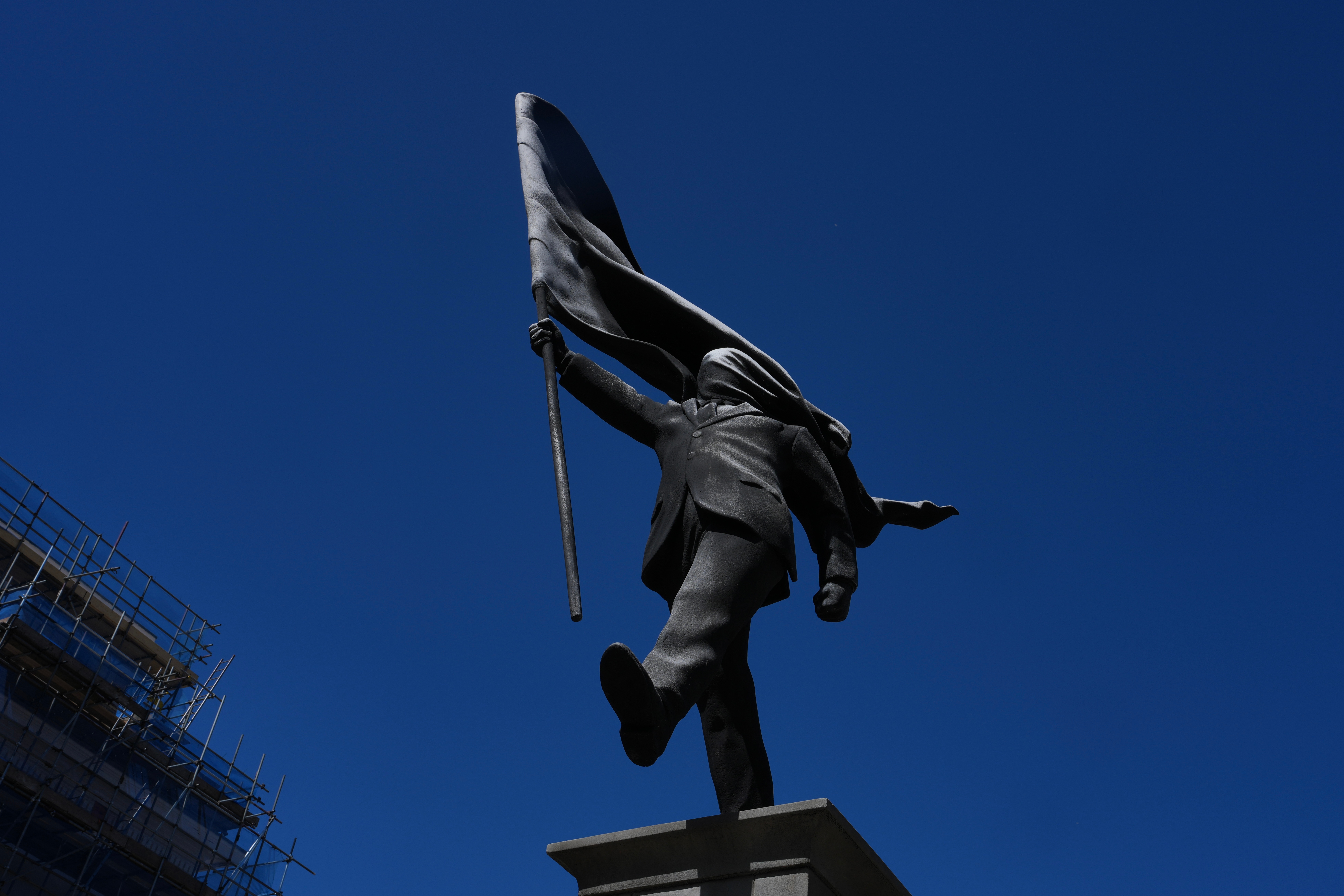 A statue of a man holding a flag covering his face, and signed 